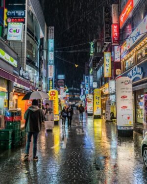 Colorful neon-lit street in Seoul, South Korea showing bustling nightlife with reflections on wet pavement.